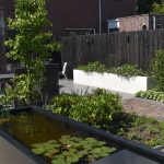 Landelijke tuin met zwarte schutting, witte bloembakken en vijver